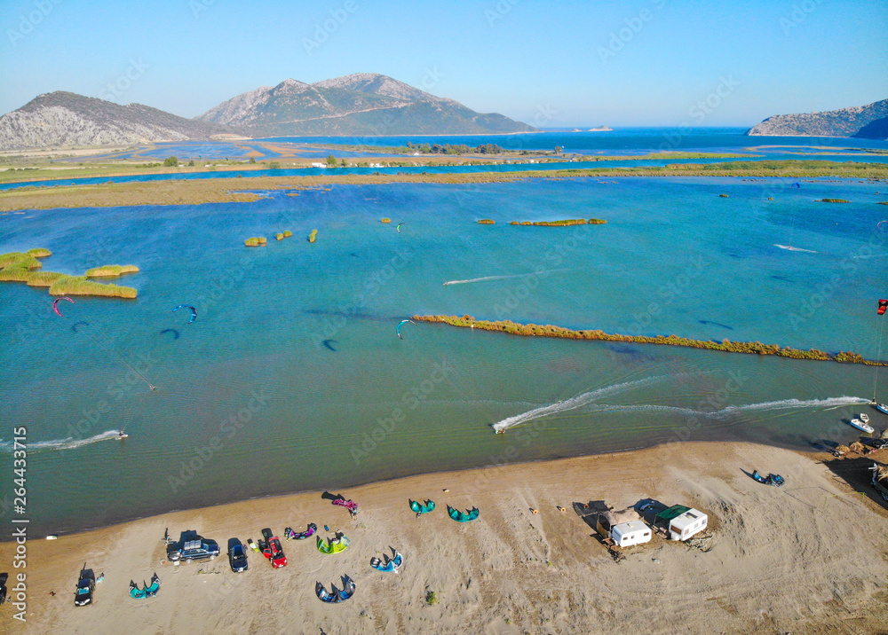 无人机：沿着沙滩飞行，风筝冲浪者在多风的海湾周围骑行。