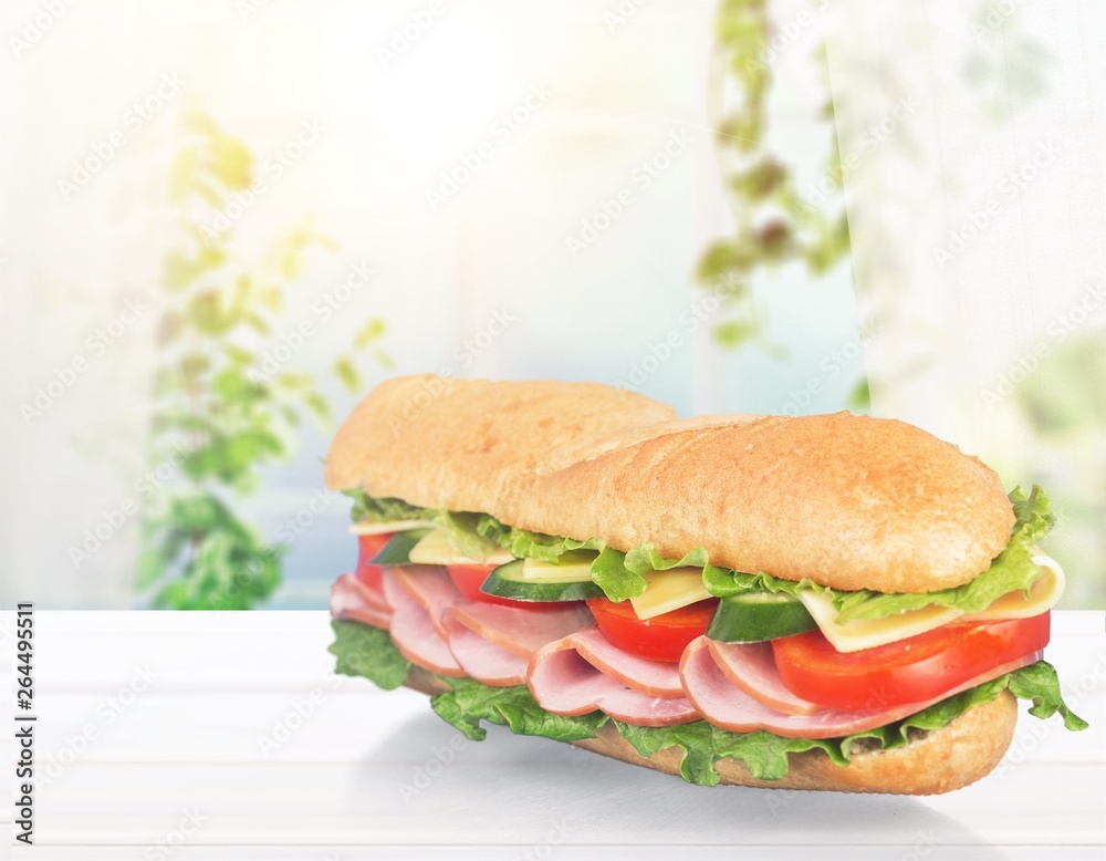 Long baguette sandwich with lettuce, vegetables, ham, and cheese on white background