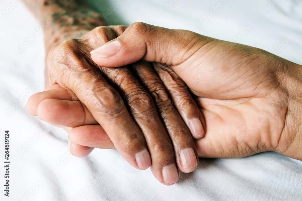 Hands of an old man with wrinkled and wrinkles on a white bed in a hospital.