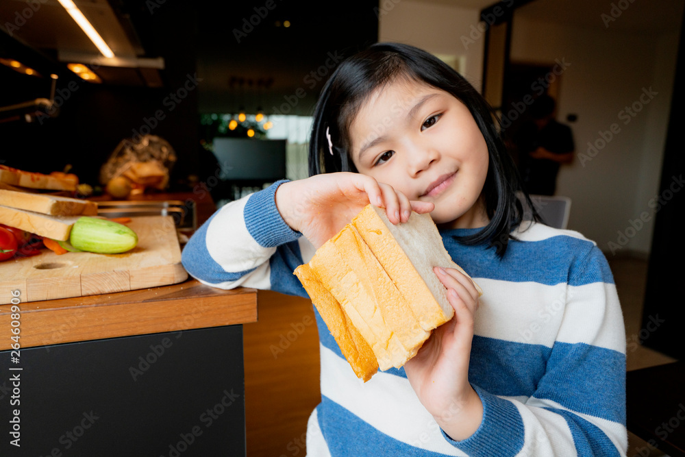 asian healthy kid girl in blue and white sweater enjoy and feel good with bread sandwish in kitchen