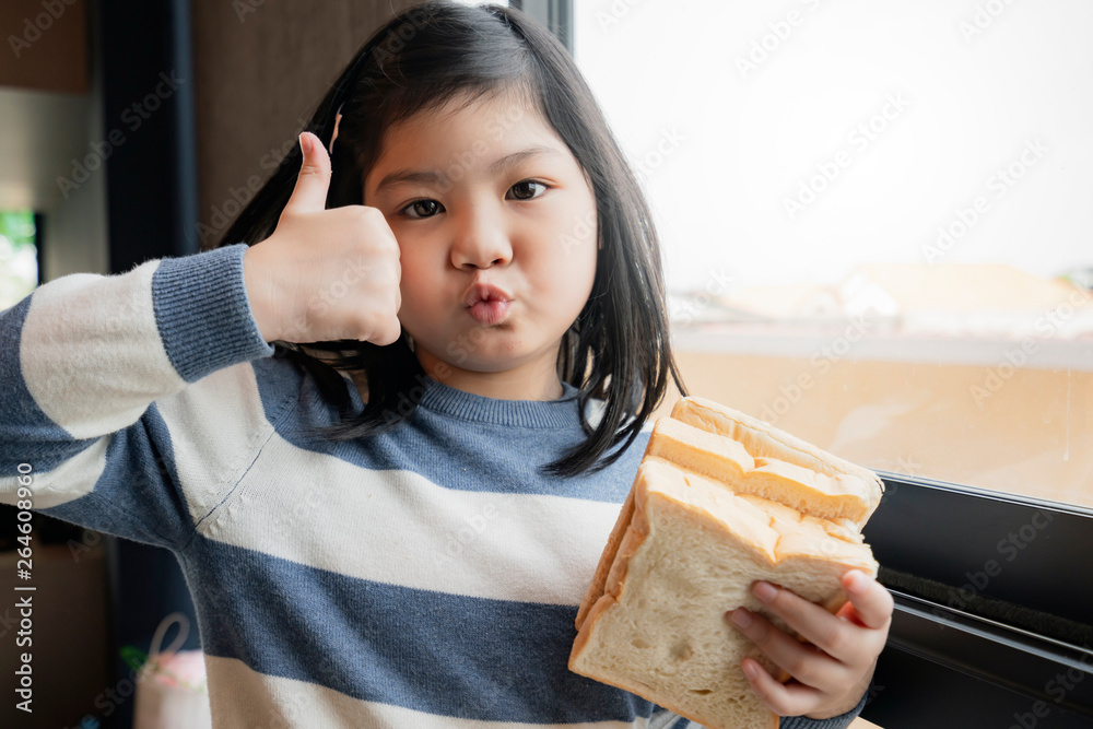 asian healthy kid girl in blue and white sweater enjoy and feel good with bread sandwish in kitchen