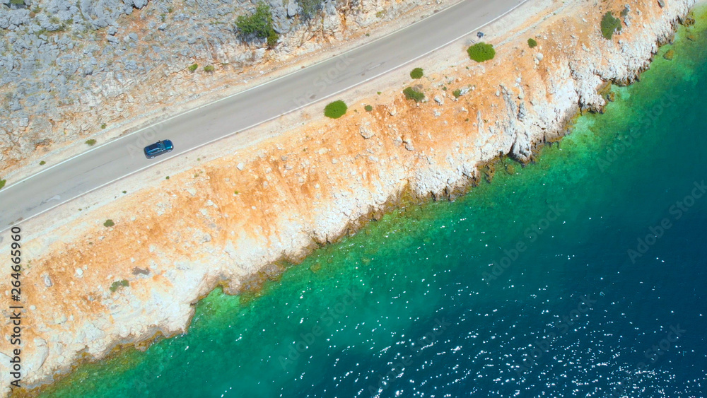 AERIAL: Flying along a tourist car cruising down empty coastal road on sunny day