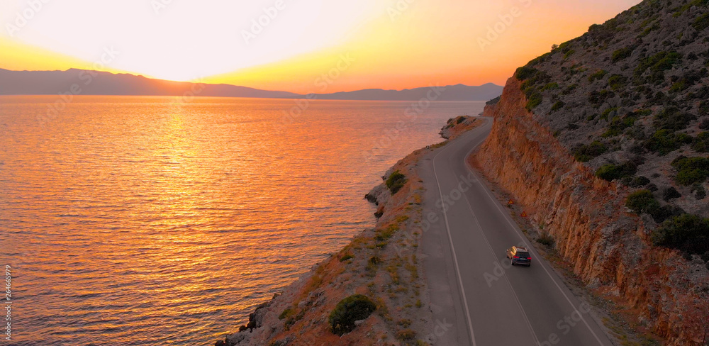 DRONE: Flying behind tourist car driving down empty road leading around island.