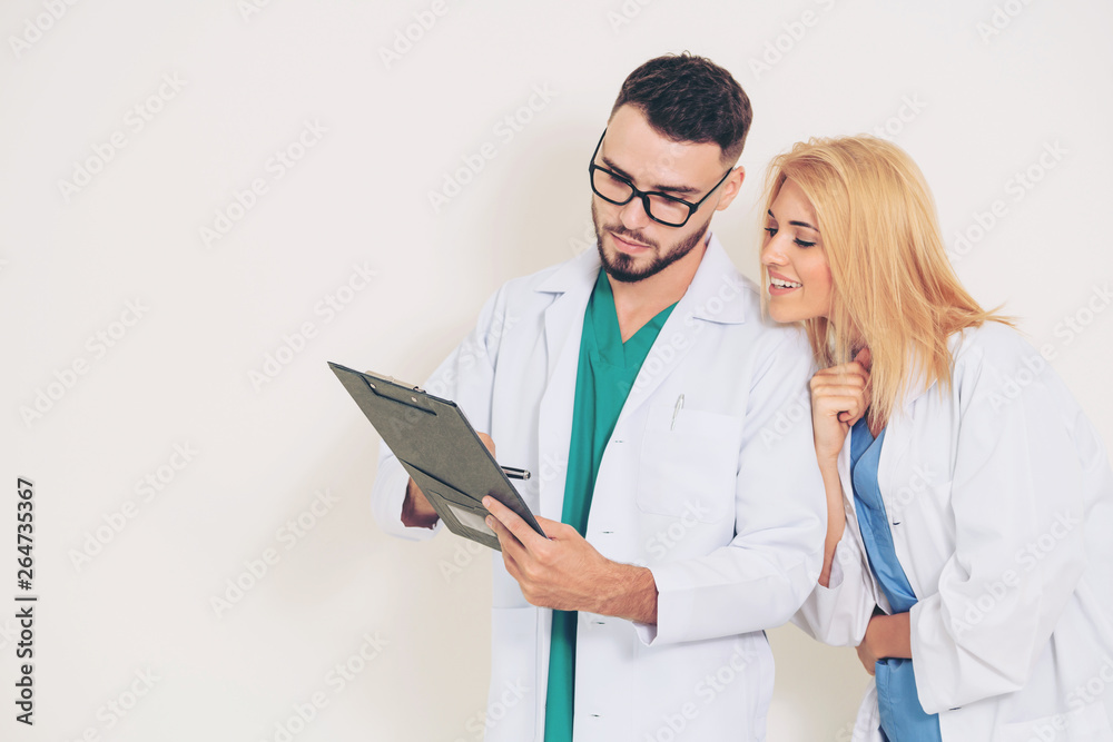 GP doctor looks at data in documents on clipboard while discussing with surgical doctor on white bac