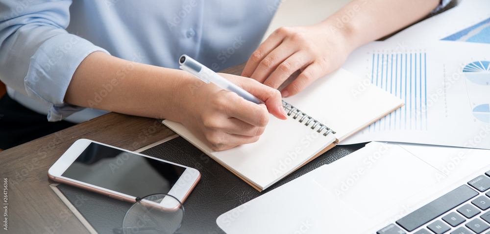 Business concept. Woman takes note for project with laptop and report in office desk. Backlighting, 