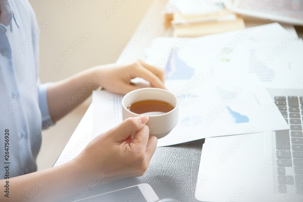 Business concept. Woman reading reports and drinking for rest in office table. Backlighting, sun gla