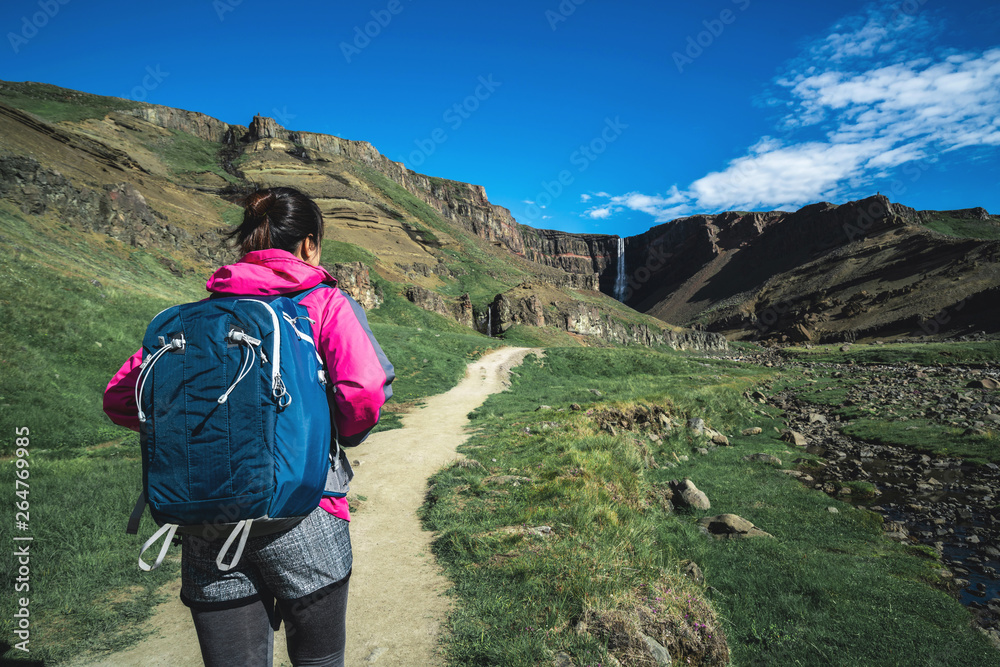 Woman traveler trekking in Icelandic summer landscape at the Hengifoss waterfall in Iceland. The wat