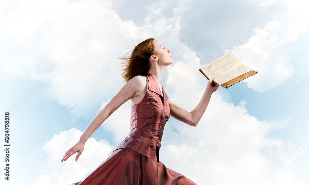 Girl against cloudy sky with opened book in palm as idea for knowledge