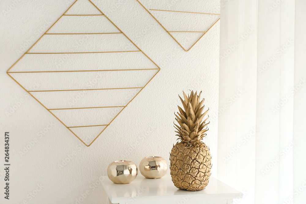 Golden pineapple with candles on table near white wall