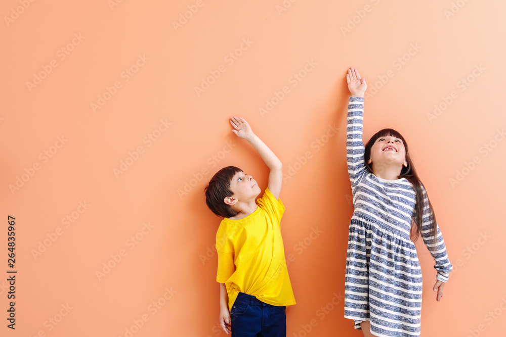 Cute little children measuring height near color wall