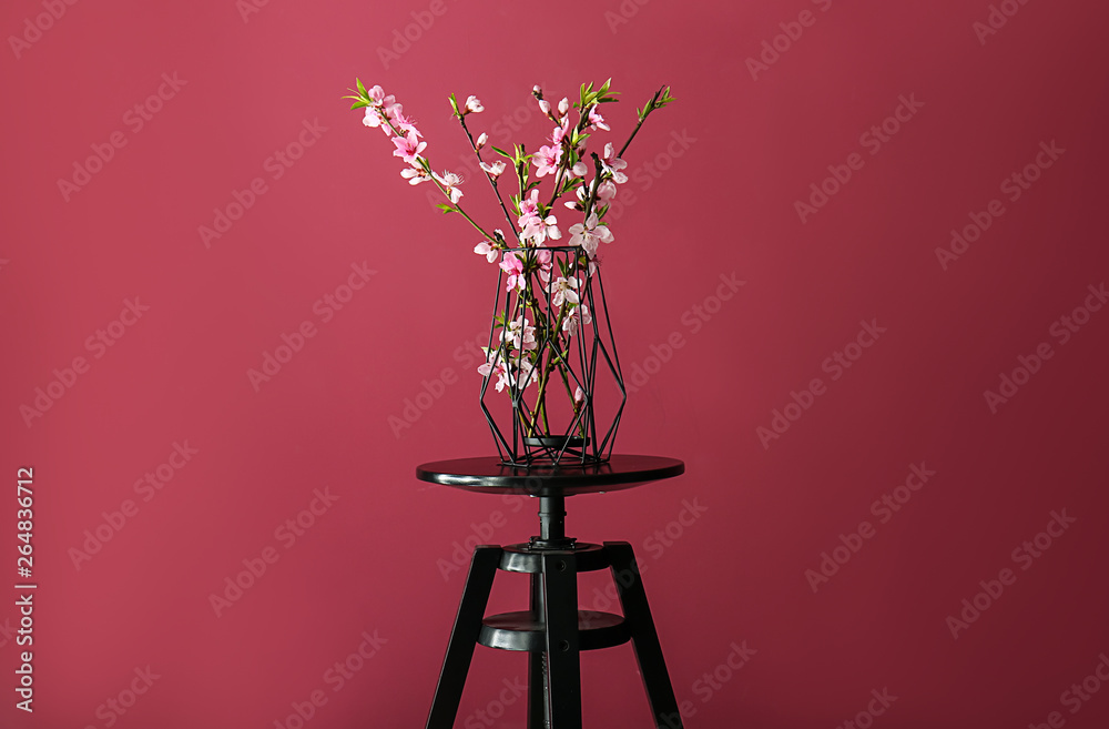 Vase with beautiful blossoming branches on table against color background