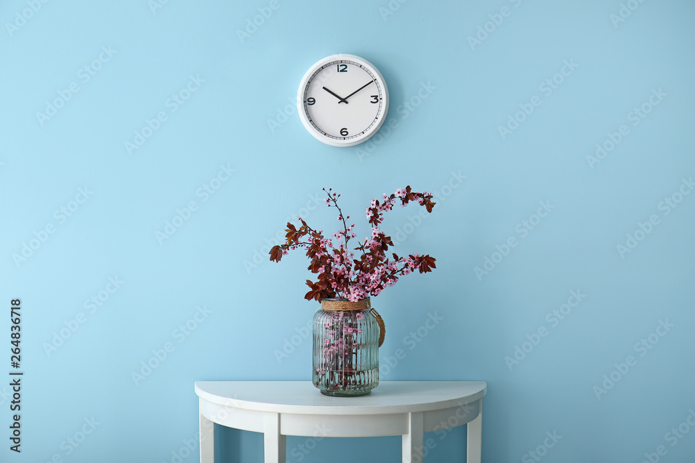 Vase with beautiful blossoming branches on table near color wall