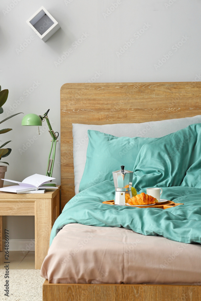 Tray with tasty breakfast on bed in interior of room