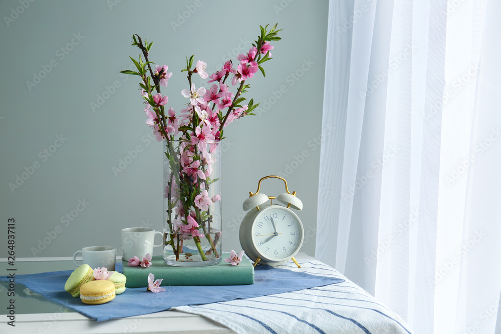 Composition with beautiful blooming branches, clock, cups and tasty macarons on table