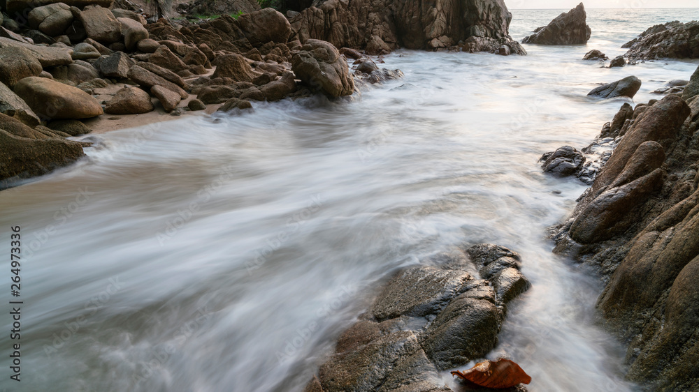 Long exposure image of  wave seascape with rock in sunset scenery background