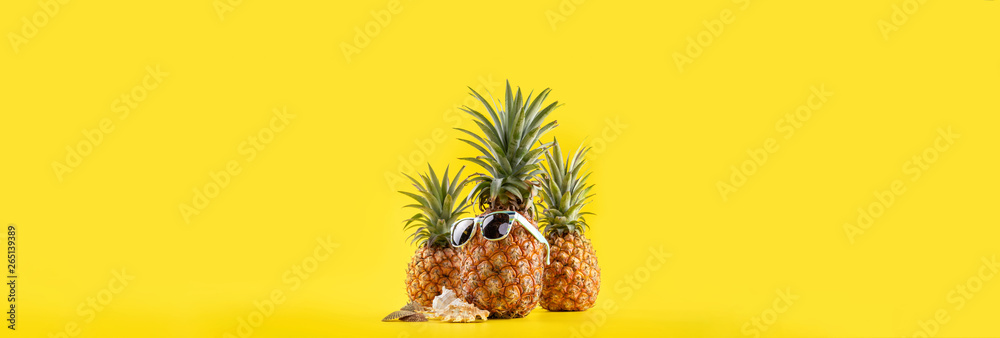 Creative pineapple looking up with sunglasses and shell isolated on yellow background, summer vacati