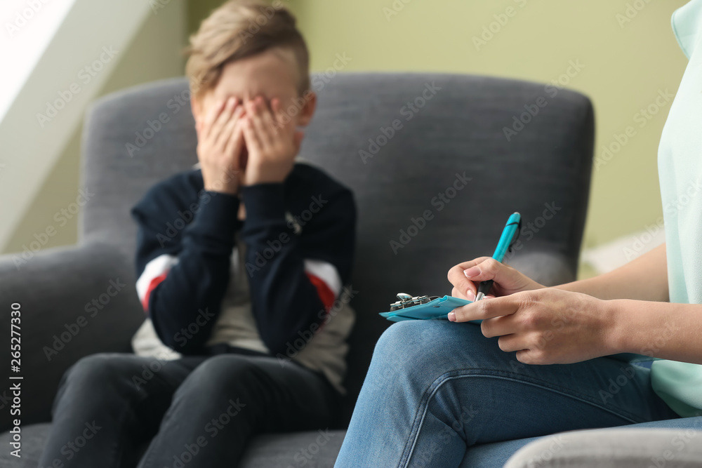 Female psychologist working with sad little boy in office