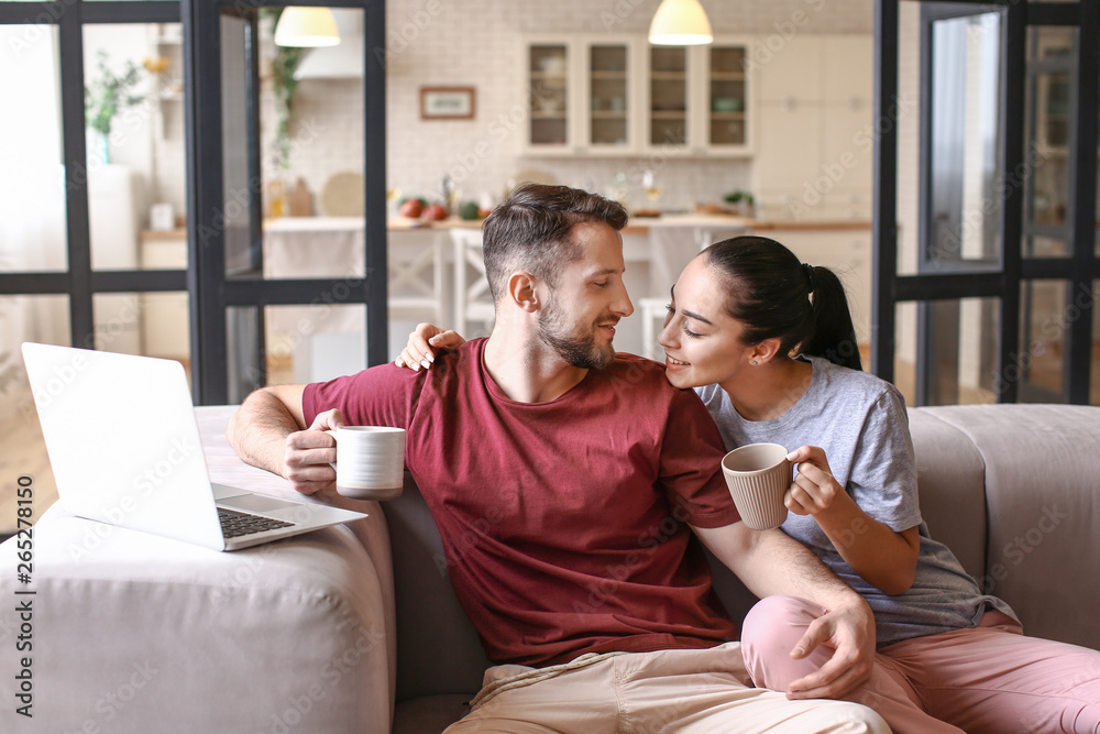 Happy young couple with laptop drinking tea at home