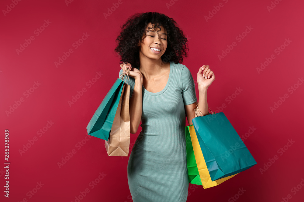 Happy African-American woman with shopping bags on color background