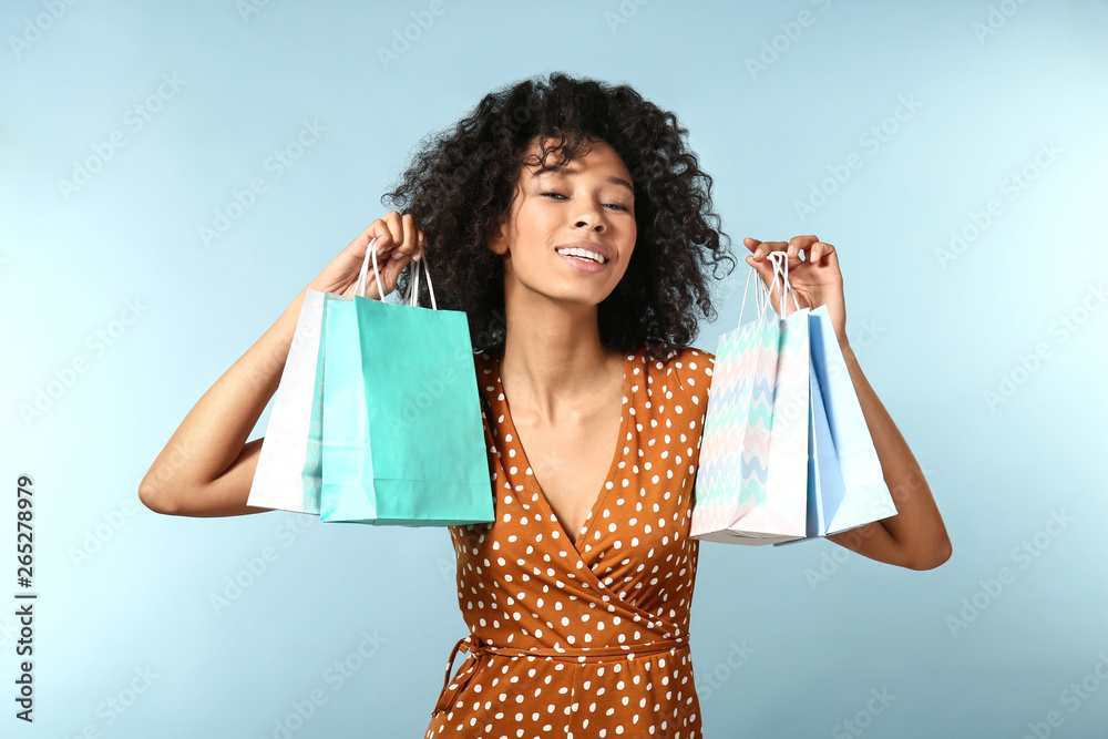 Happy African-American woman with shopping bags on color background