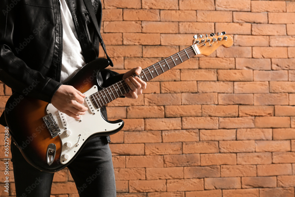 Handsome young man playing guitar against brick wall