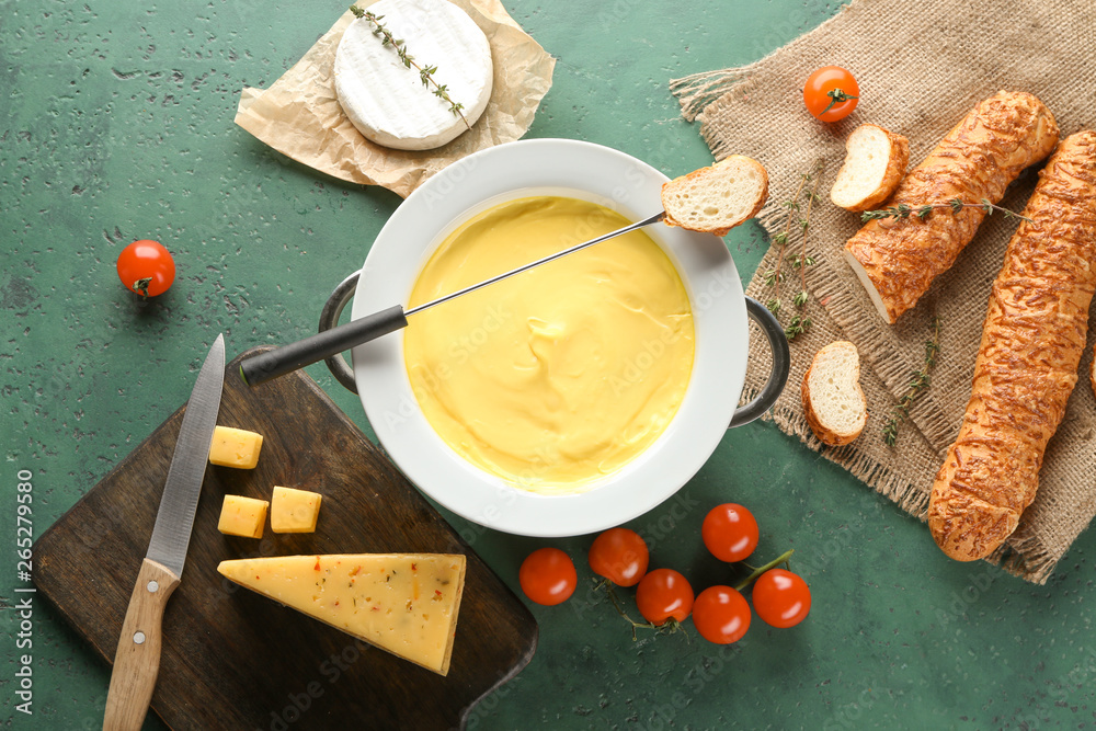 Cheese fondue with snacks on color background