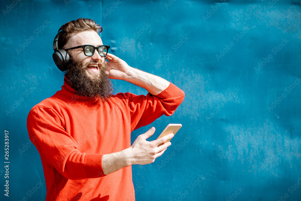 Portrait of a stylish man dressed in red sweater enjoying music with headphones and smart phone on t