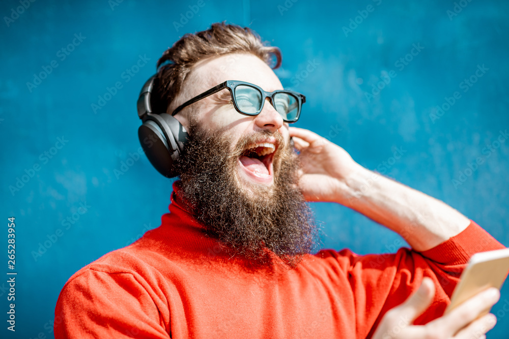 Portrait of a stylish man dressed in red sweater enjoying music with headphones and smart phone on t