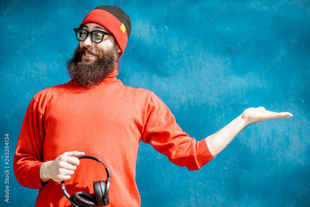 Portrait of a stylish bearded man dressed in red sweater and hat showing on the blue background