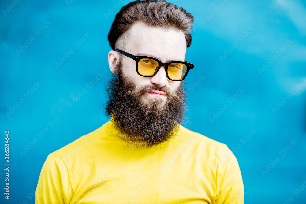 Close-up portrait of a confused bearded man in yellow sweater and sunglasses on the blue background