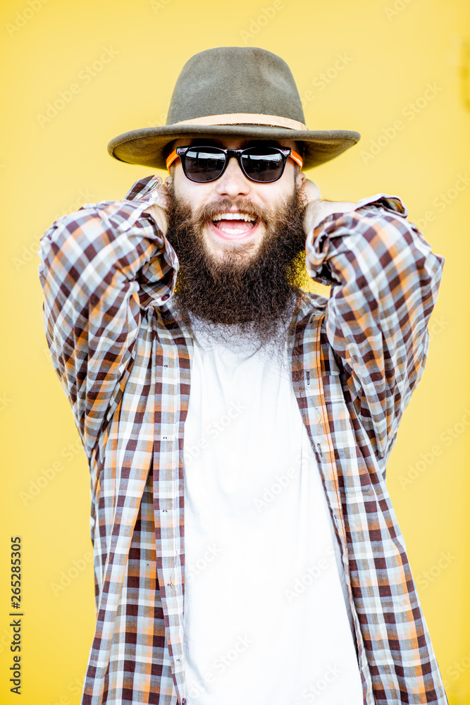 Portrait of a cool stylish man in shirt and hat posing on the bright yellow background