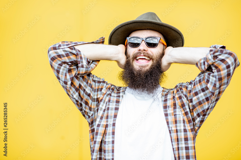 Portrait of a cool stylish man in shirt and hat posing on the bright yellow background