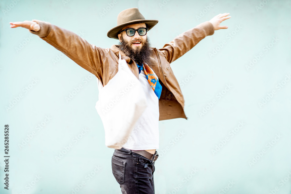 Portrait of a stylish man dressed in jacket, hat and scarf with bag on the turquoise background outd