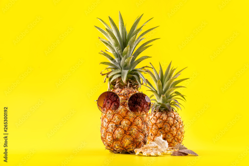 Creative pineapple looking up with sunglasses and shell isolated on yellow background, summer vacati