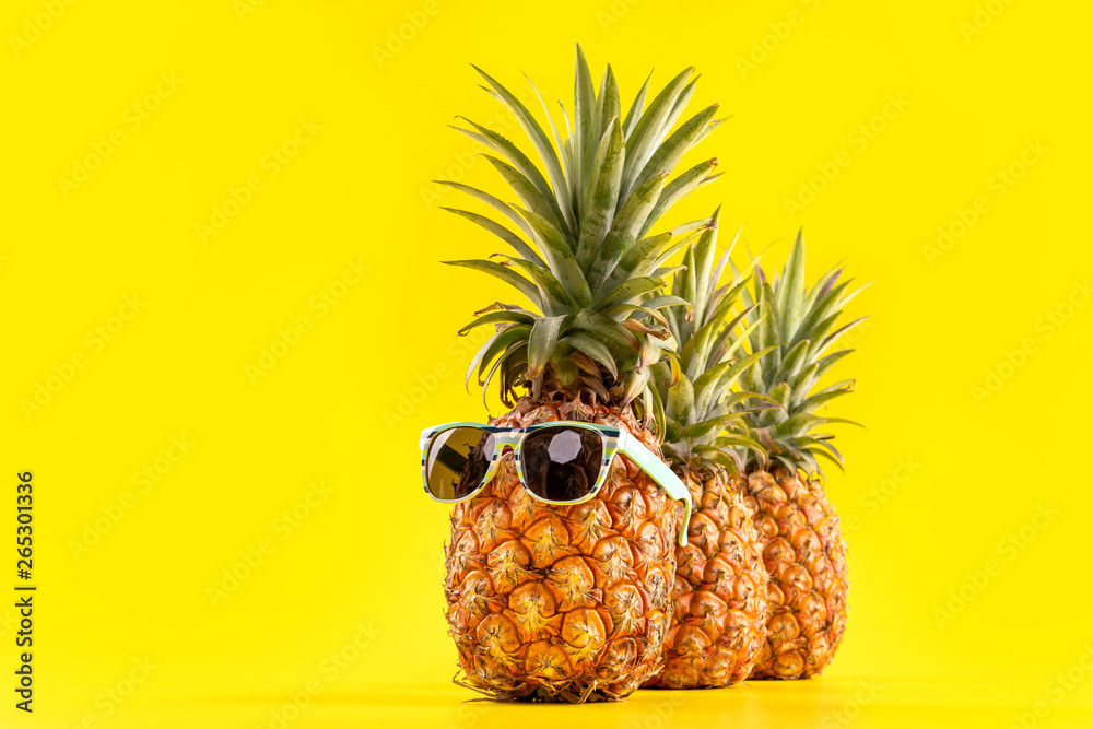 Creative pineapple looking up with sunglasses and shell isolated on yellow background, summer vacati