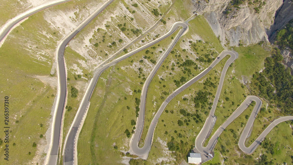 AERIAL: Tourist car driving up a winding asphalt road in the sunny Dolomites.