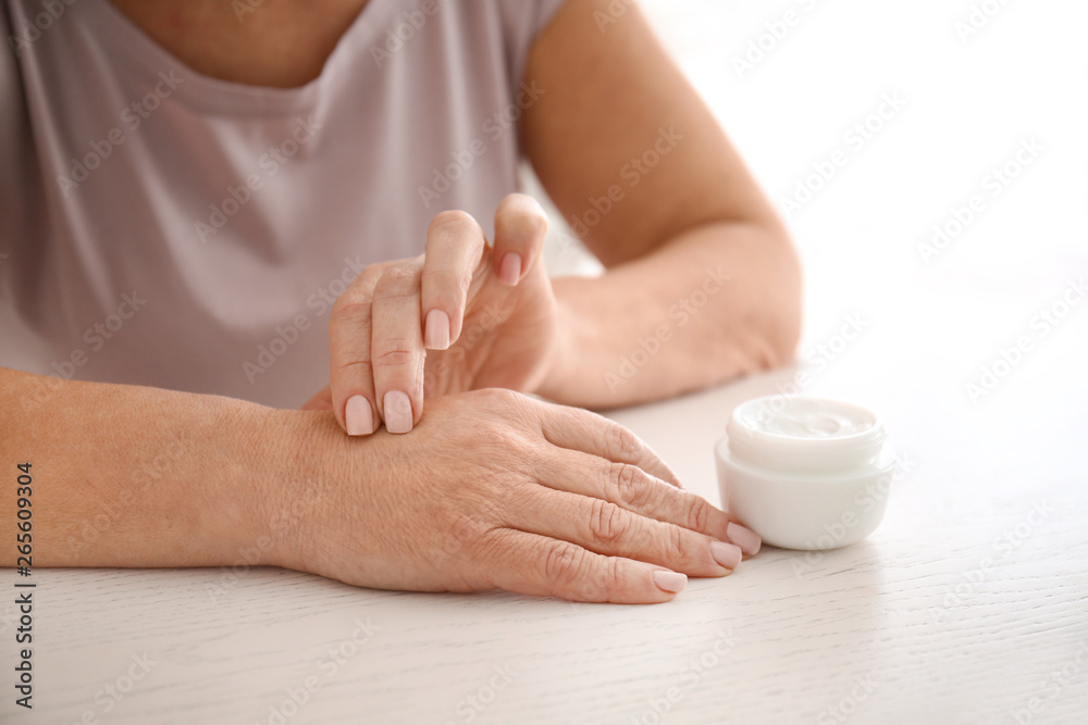 Mature woman applying hand cream at home, closeup