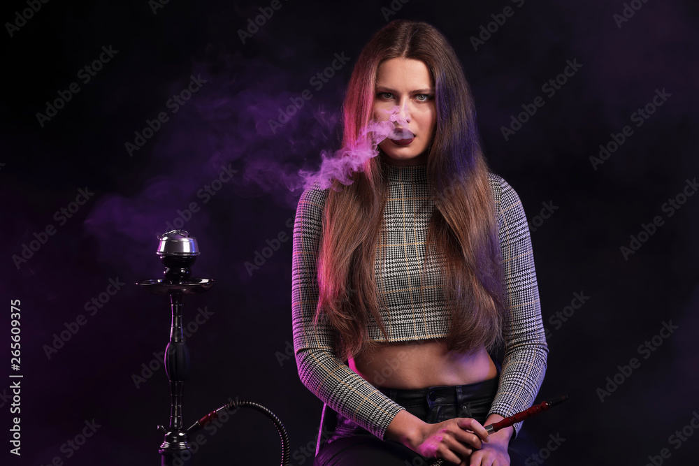 Young woman smoking hookah on dark background