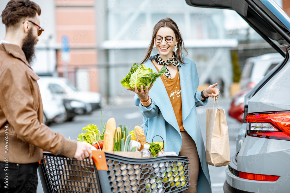 年轻时尚的情侣带着装满新鲜食物的购物车，出门就把产品装进车里