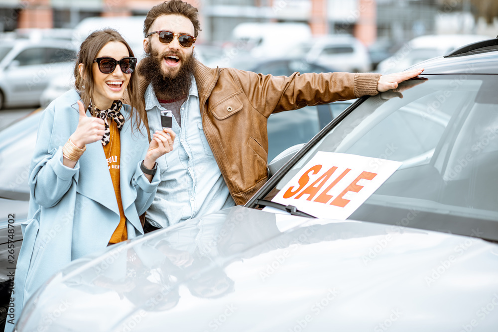 Portrait of a happy couple standing together as owners of a new car on the open ground of the dealer