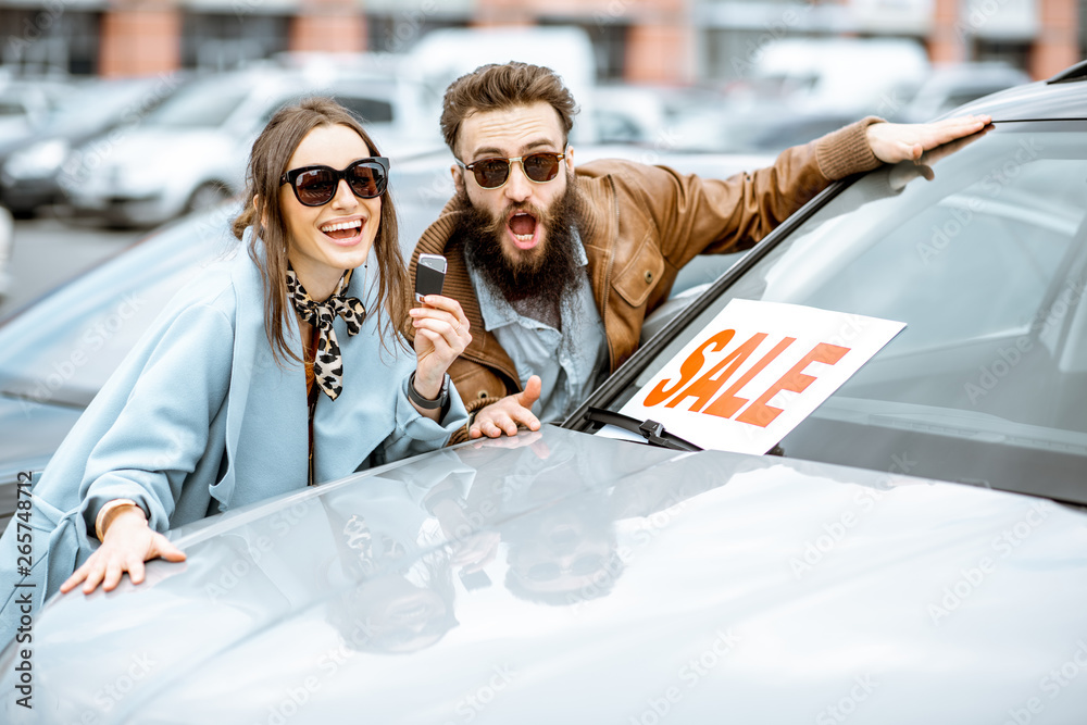 Portrait of a happy couple standing together as owners of a new car on the open ground of the dealer