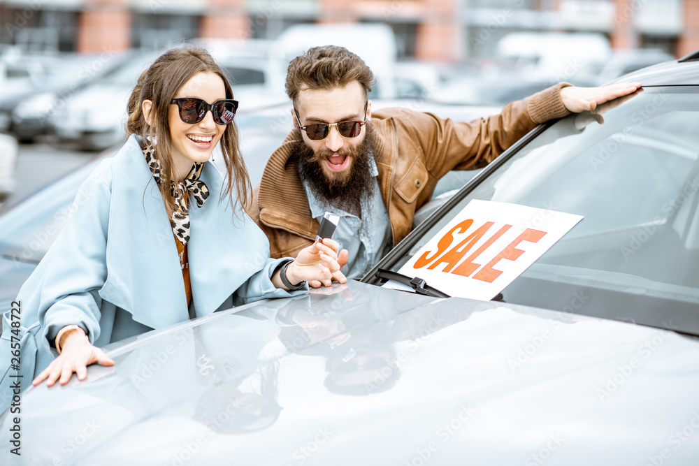 Portrait of a happy couple standing together as owners of a new car on the open ground of the dealer