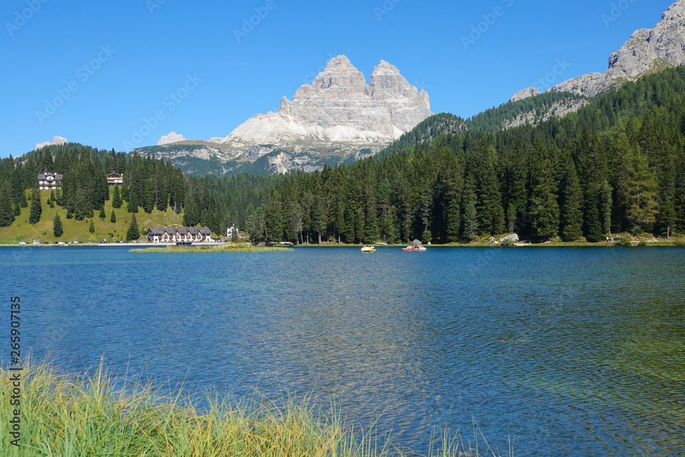 Tourists in boats wandering around the tranquil lake in the sunny Dolomites.