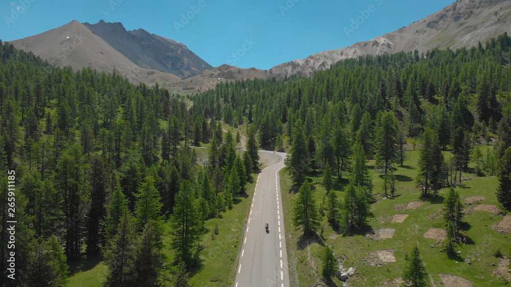 AERIAL: Motorcycle riders cruising along asphalt road leading through the woods.