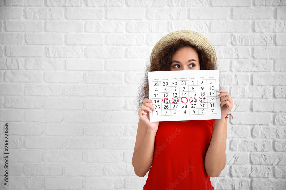 African-American woman holding calendar with marked days of menstruation on white background