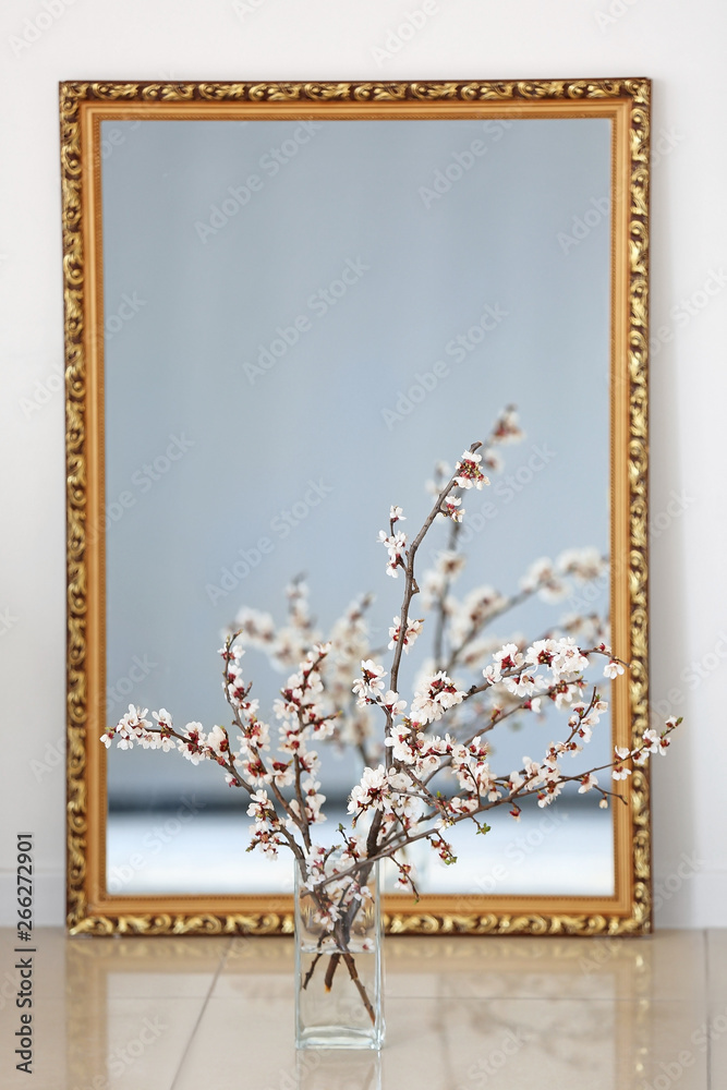 Vase with beautiful blossoming branches and mirror on floor in room