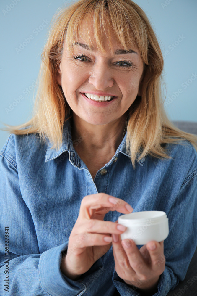 Mature woman with jar of cream on color background