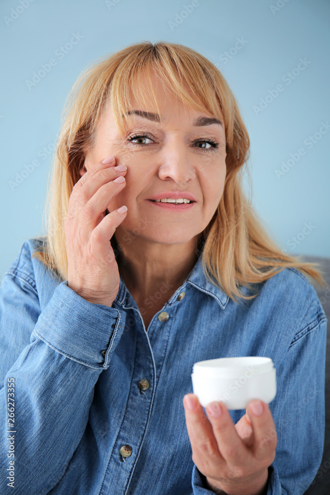 Mature woman with jar of cream on color background