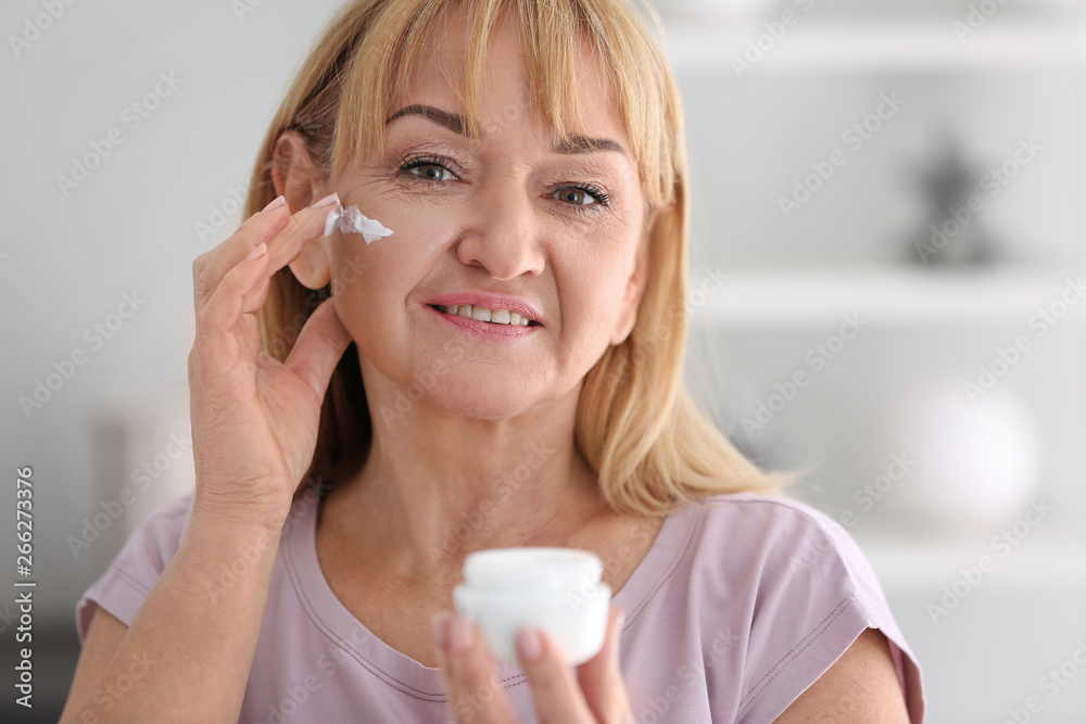 Mature woman applying facial cream at home