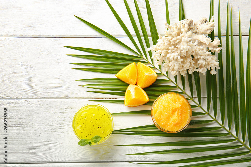 Bowls with body scrub, coral and palm leaf on white wooden background